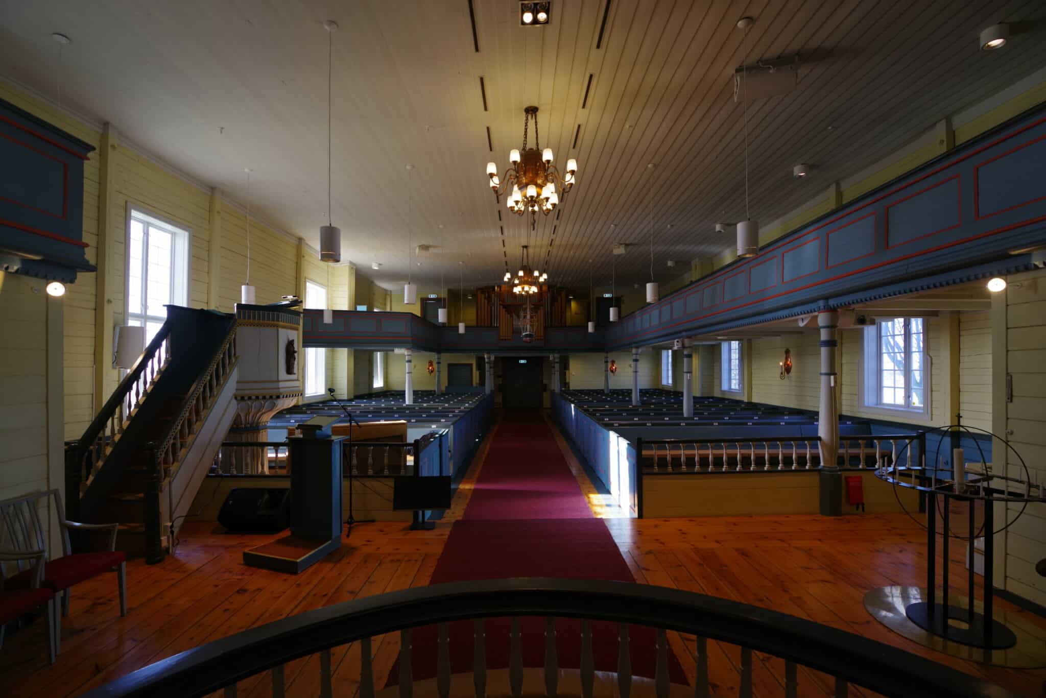 Innsiden av en kirke sett fra alterområdet mot inngangen. En rød løper strekker seg nedover midtgangen mellom de blå kirkebenkene. Til venstre ses en hvit prekestol med trapp, og i bakgrunnen ser man kirkeorgelet på galleriet.